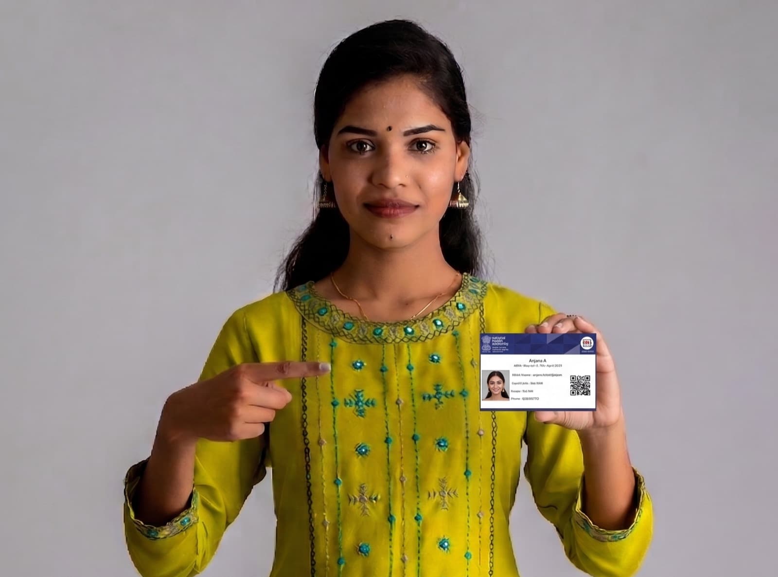 A young Indian woman in a yellow kurta smiling and pointing to her ABHA health ID card